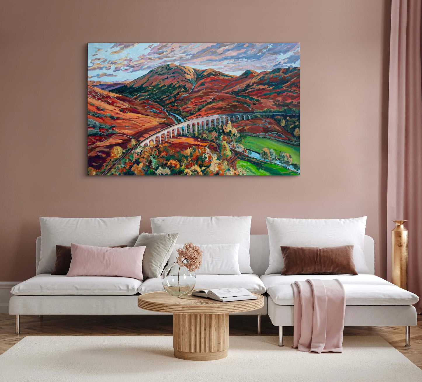 The famous railway used to take young wizards to school, painting of iconic Scottish highlands, near Ft William and the close to where the Jacobite Rebellion happened set in a warm living room with light beige/ peach walls with a cream couch with colored pillows and a small circular coffee table with vase and book.