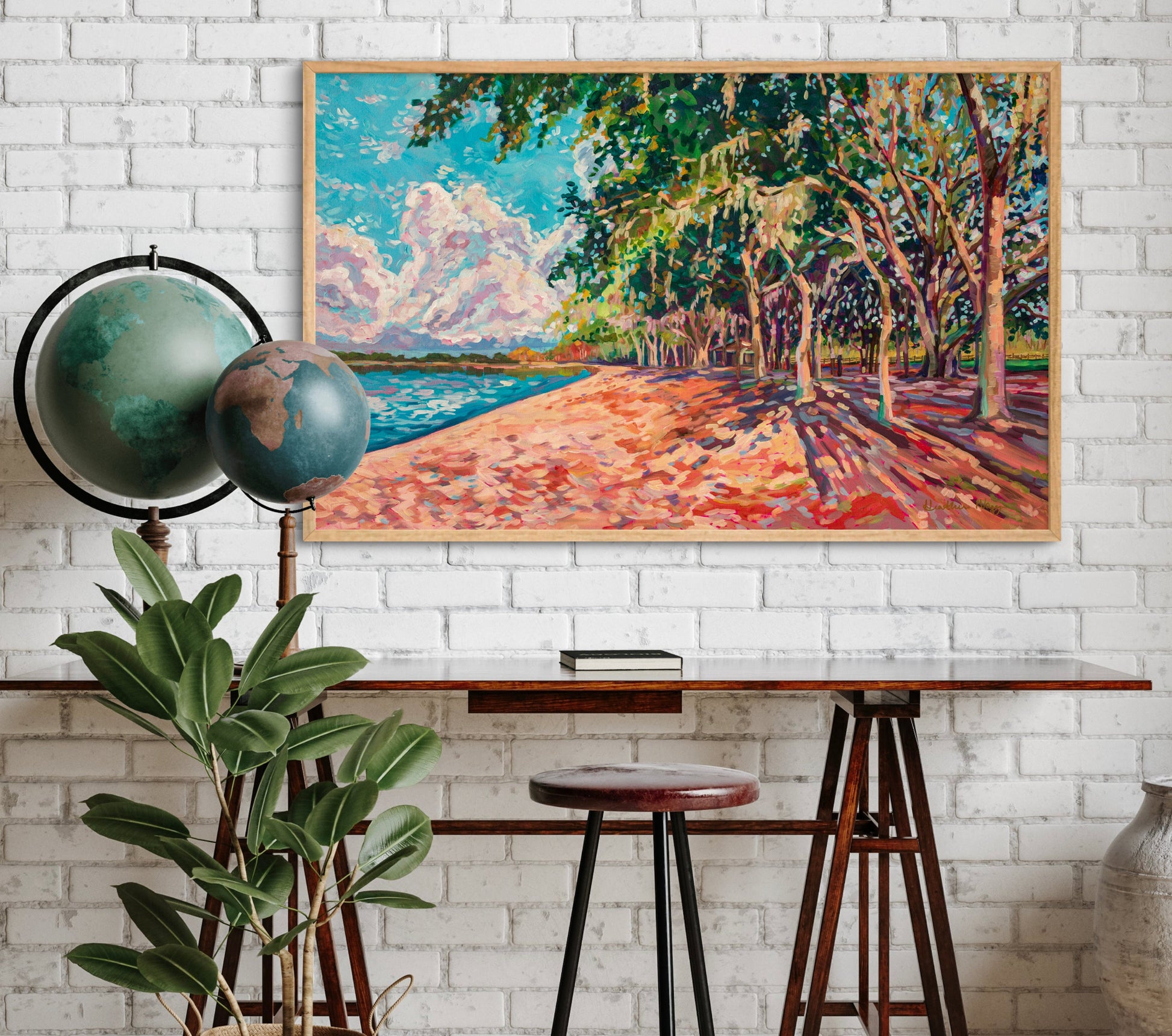 modern office with minimal desk and globes, plant, and white brick wall with landscape impressionist painting of oak trees along a lake.