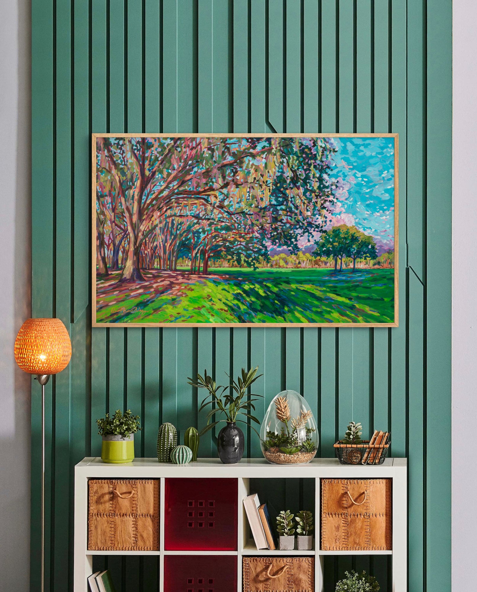 Chisholm Park landscape painting by Heather Nagy on green wall above a shelf with plants and bins.