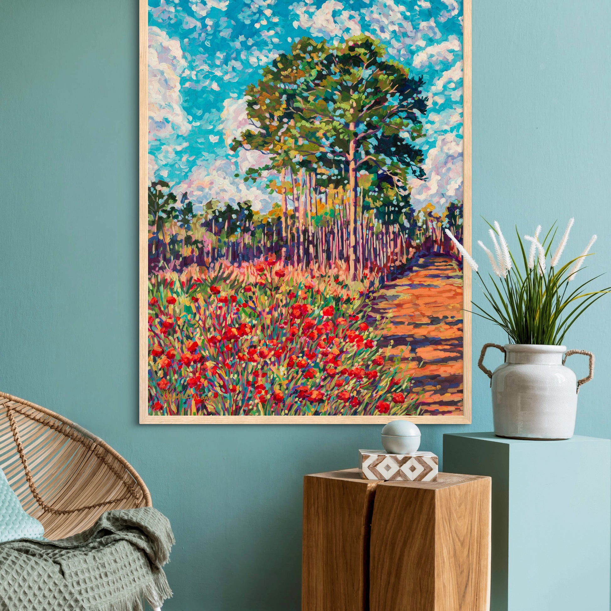 chair and two stands with decor with large landscape painting of pine trees and flowers on light teal wall in background.