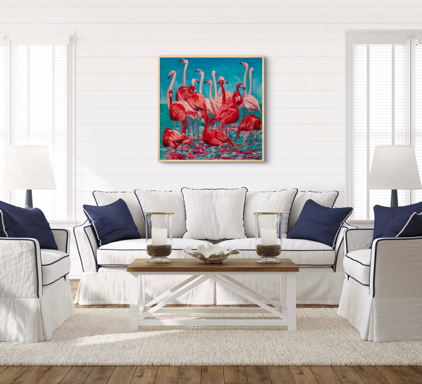 fun tropical painting of a grouping of several flamingos in the water over a couch in a white living room with navy and wood accents.