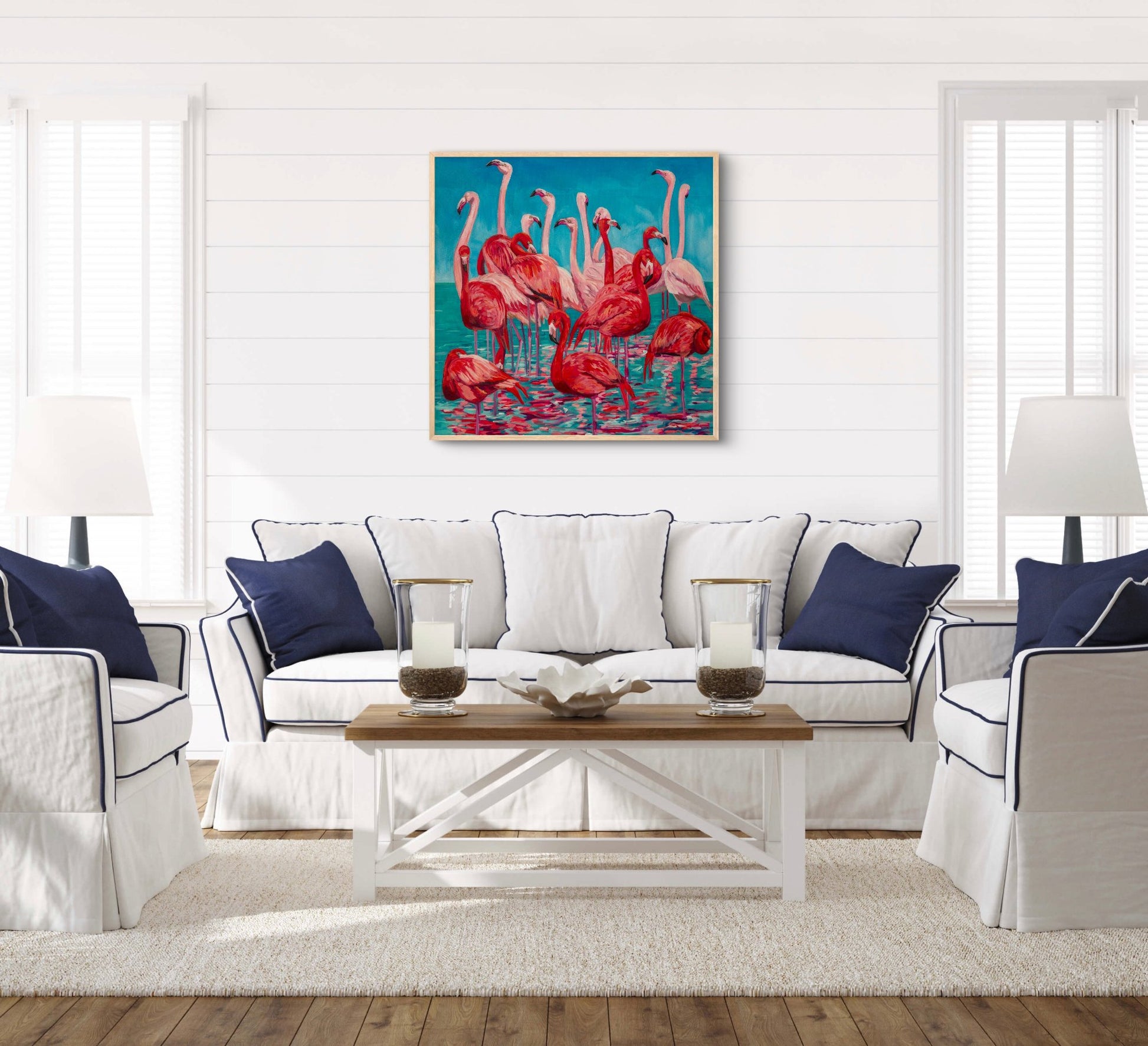 fun tropical painting of a grouping of several flamingos in the water over a couch in a white living room with navy and wood accents.