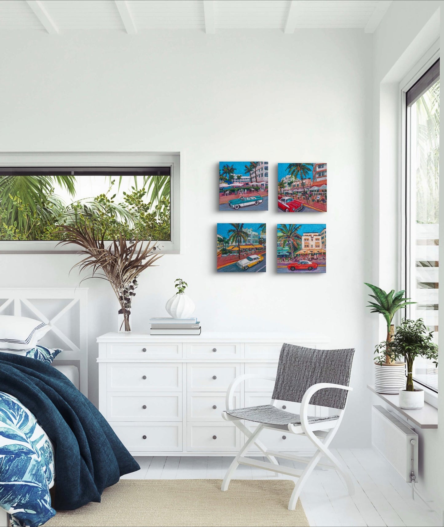 bright airy white bedroom with palm bedding and grouping of 4 square small paintings of historic iconic south beach miami each with art deco hotel and a classic car.