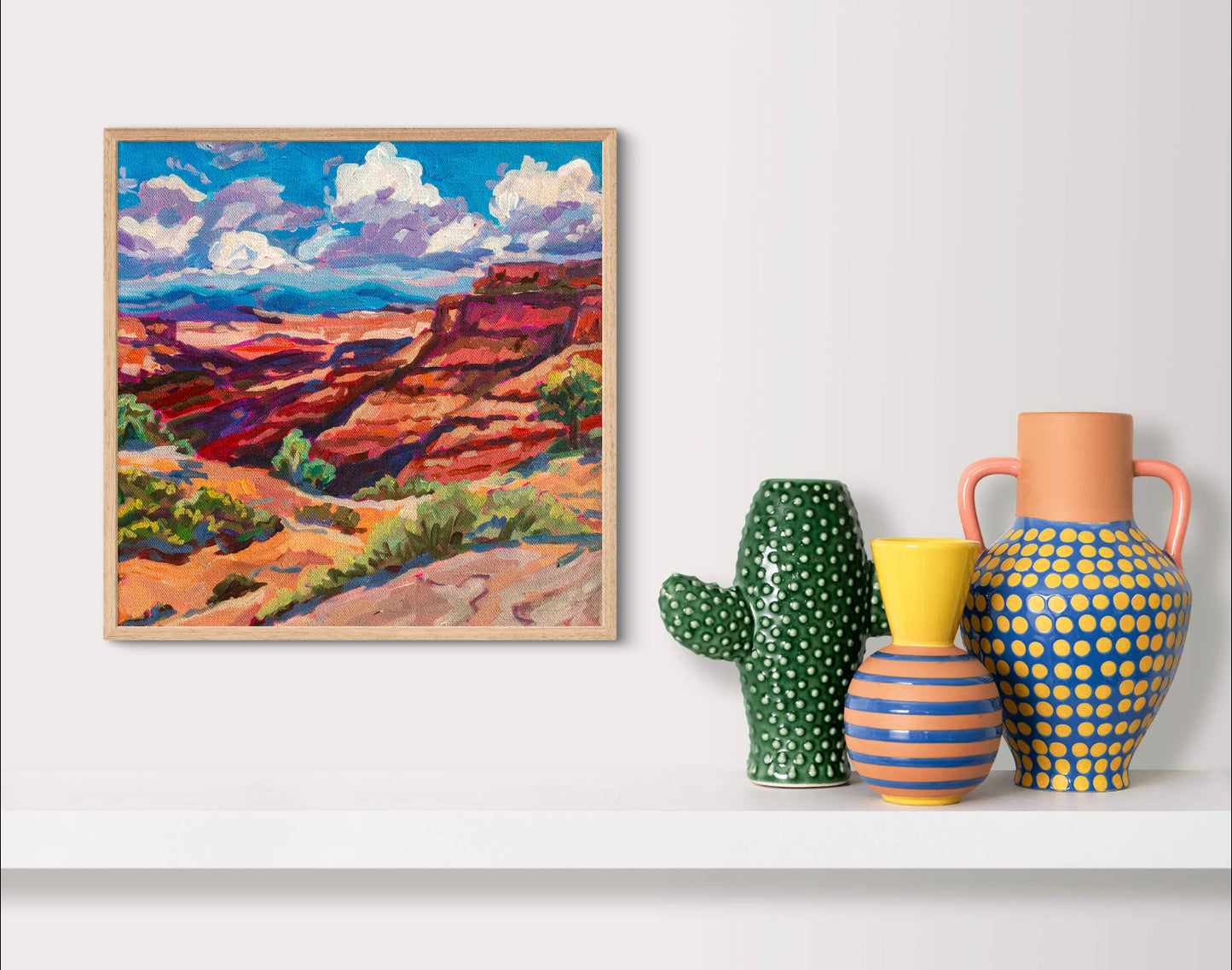 Modern landscape painting of Canyonlands national park in moab Utah above shelf with colorful pottery.