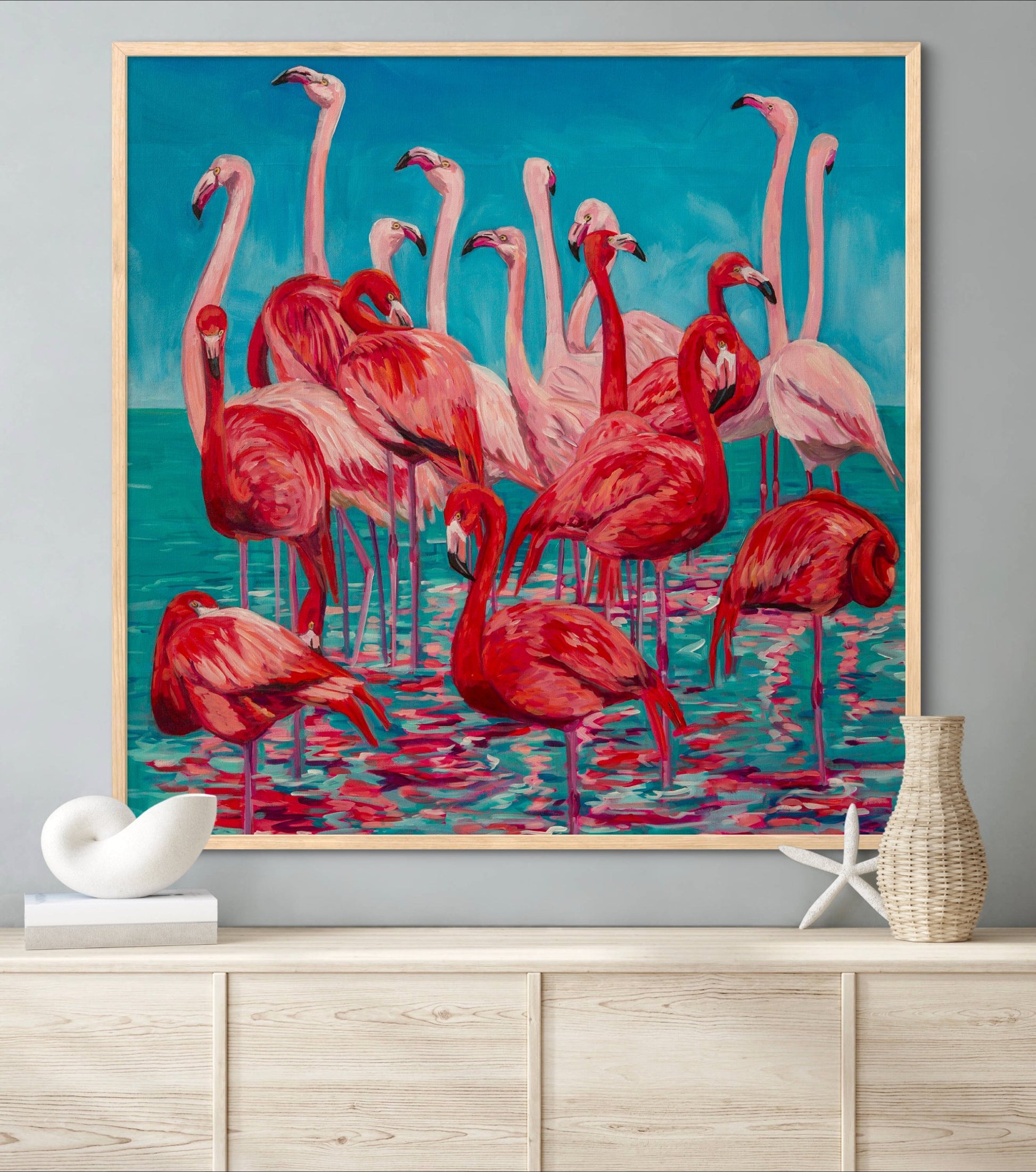 large painting with pinks, corals, reds, and teals of flamingos above a pale wood shelf with seashells.