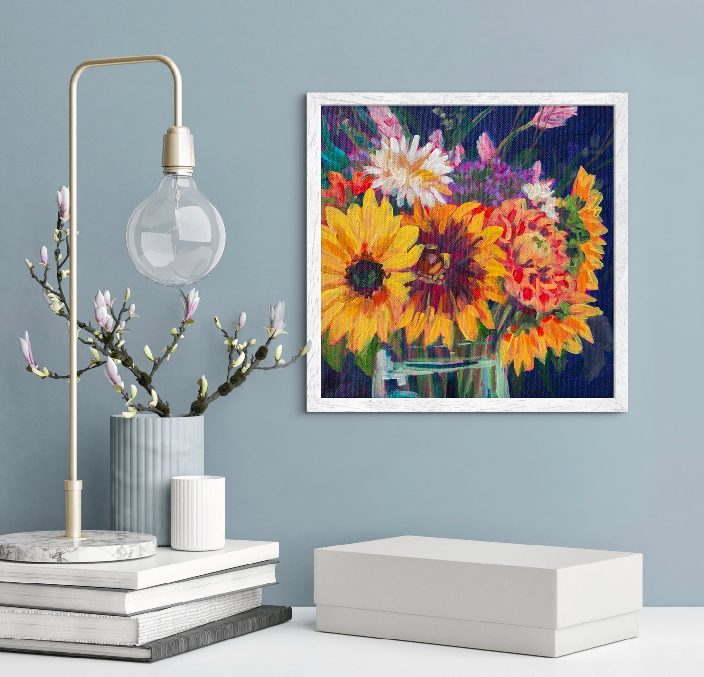 bright sunflower floral still life painting on wall above shelf with neutral decor of vases and books and a lamp.