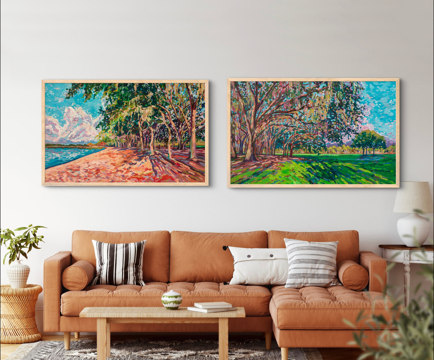 Living room with rust orange couch and neutral pillows and tables with two large horizontal paintings on the wall showing natural park landscapes with greens, blues and oranges.