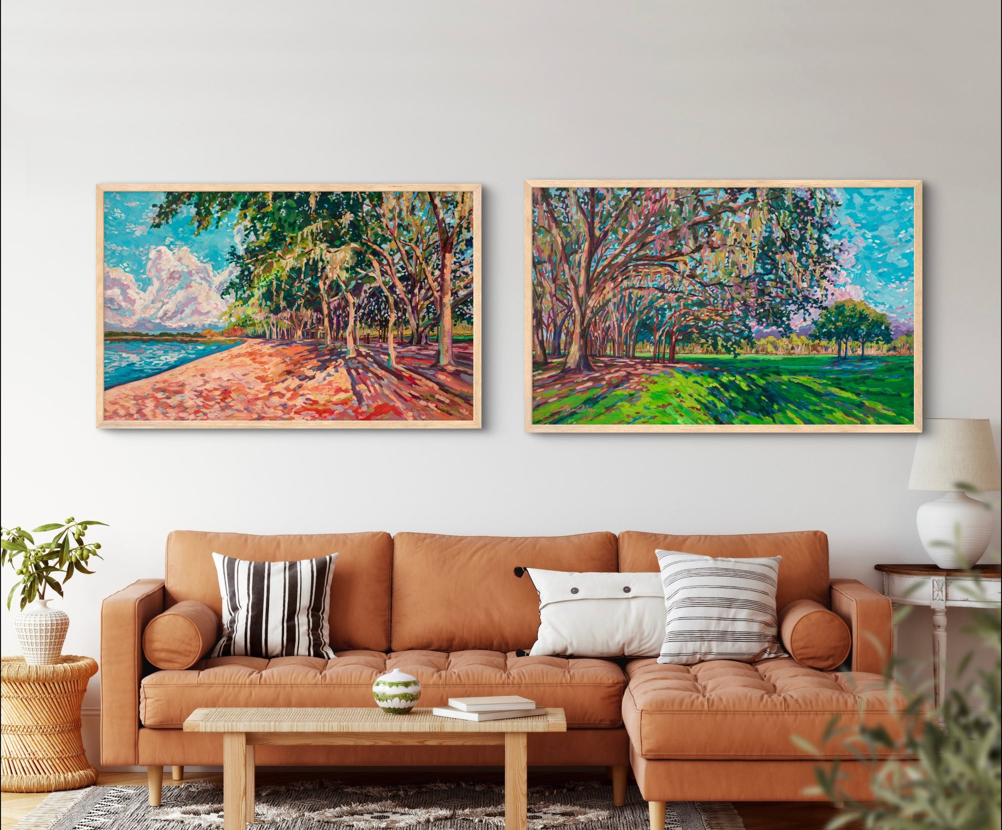 Living room with rust orange couch and neutral pillows and tables with two large horizontal paintings on the wall showing natural park landscapes with greens, blues and oranges.
