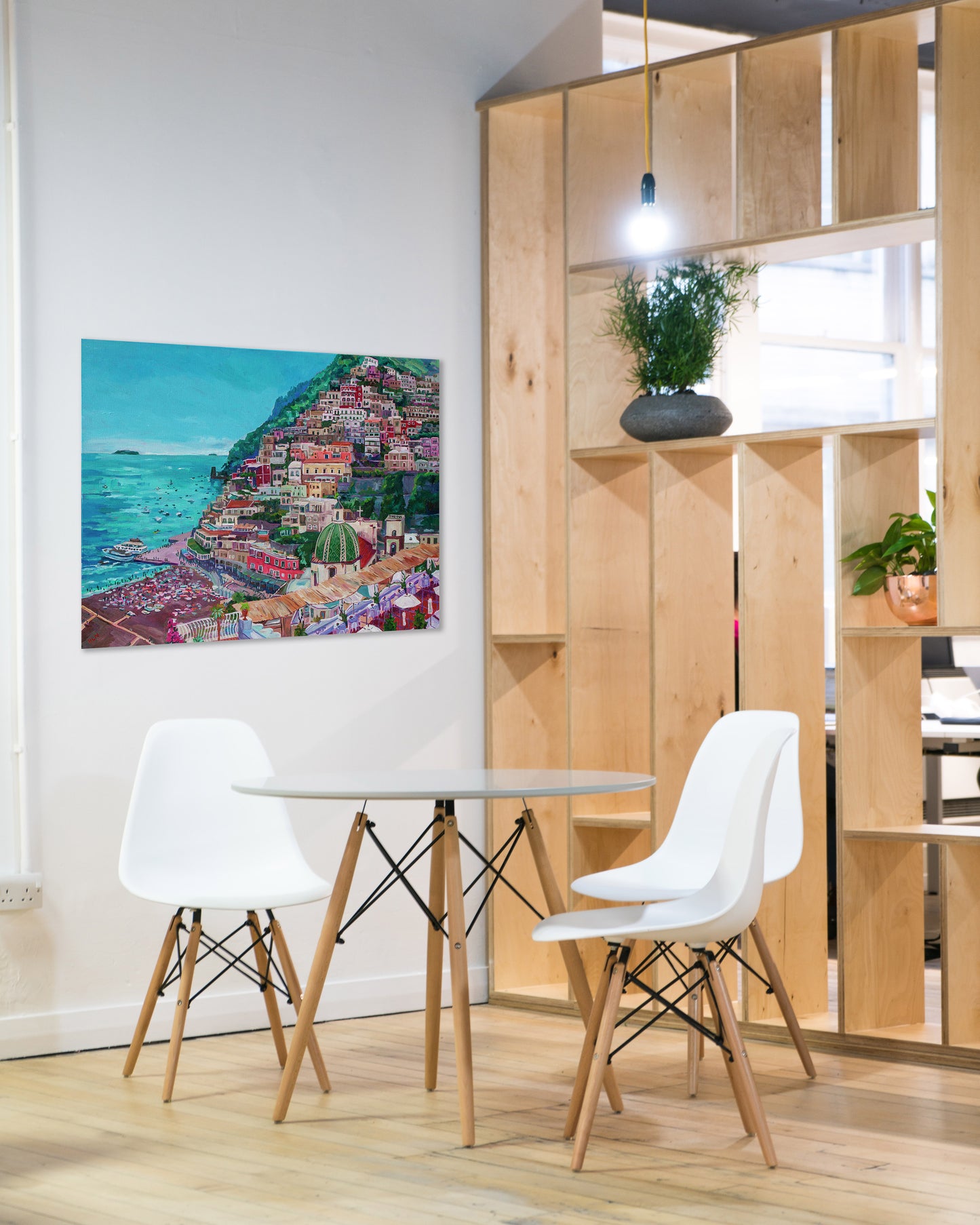 View of Summer in Positano painting on the wall of a dining room or office break room setting with table and shelf