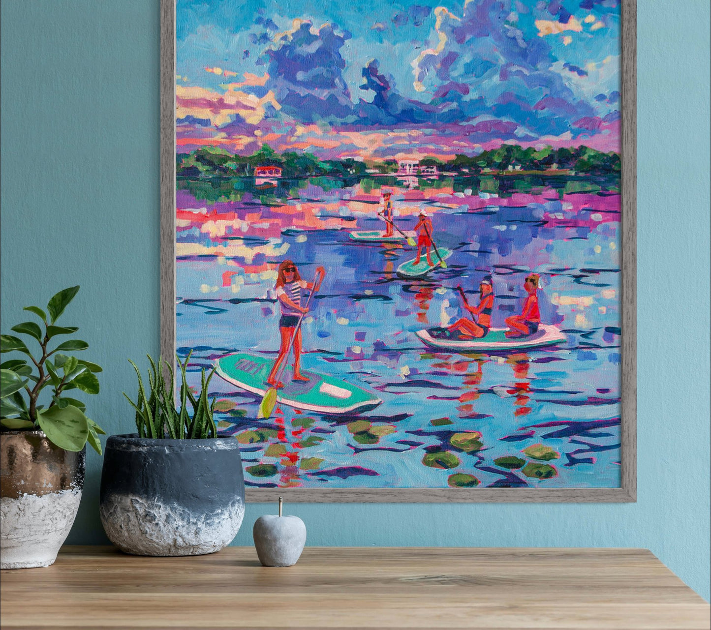 Paddle boarders on lake at sunset impressionist painting on wall with shelf and stone vases and plants