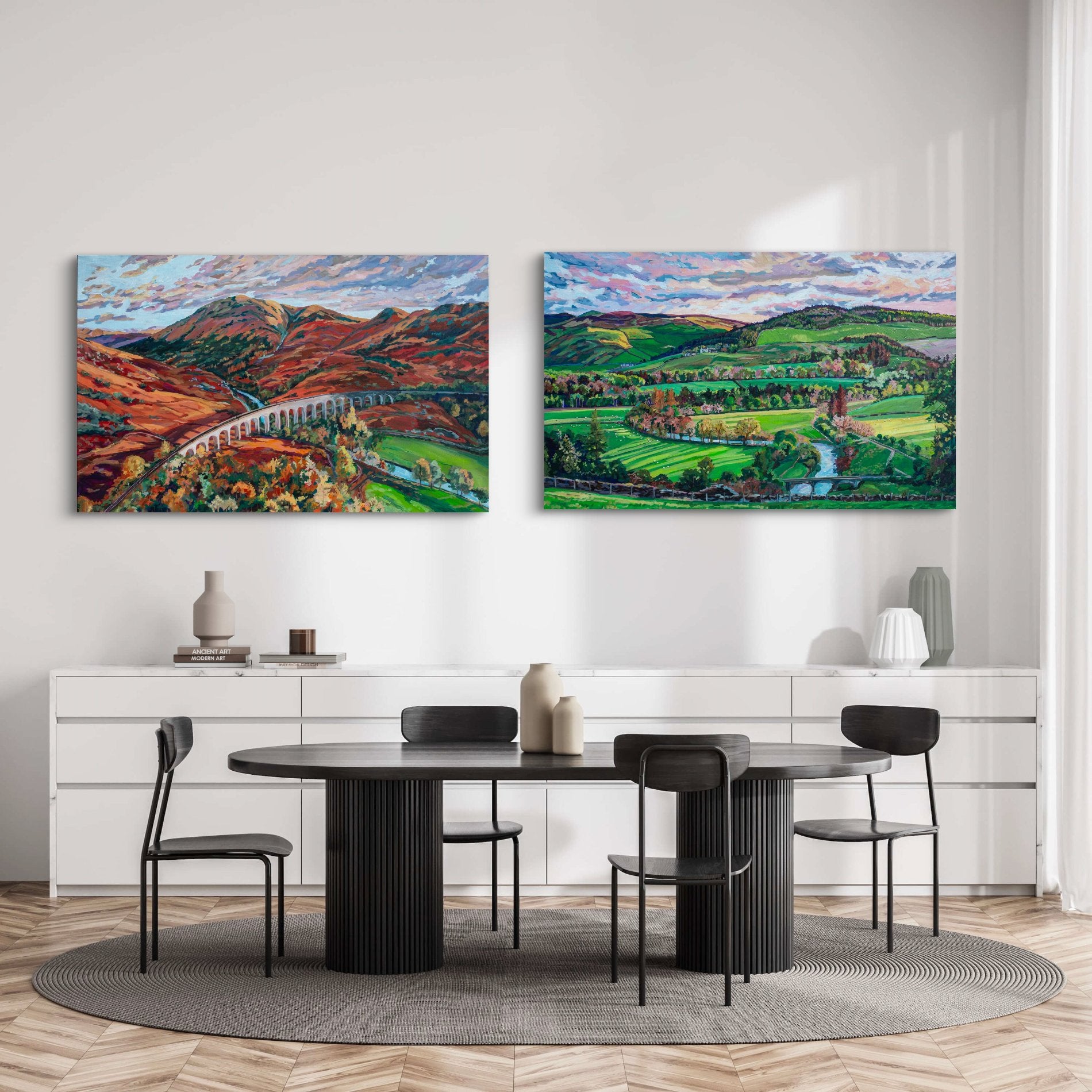 Two dramatic landscape paintings showing rolling hills and in Scotland on wall of minimalist dining room with white credenzas and modern black table and simple chairs.