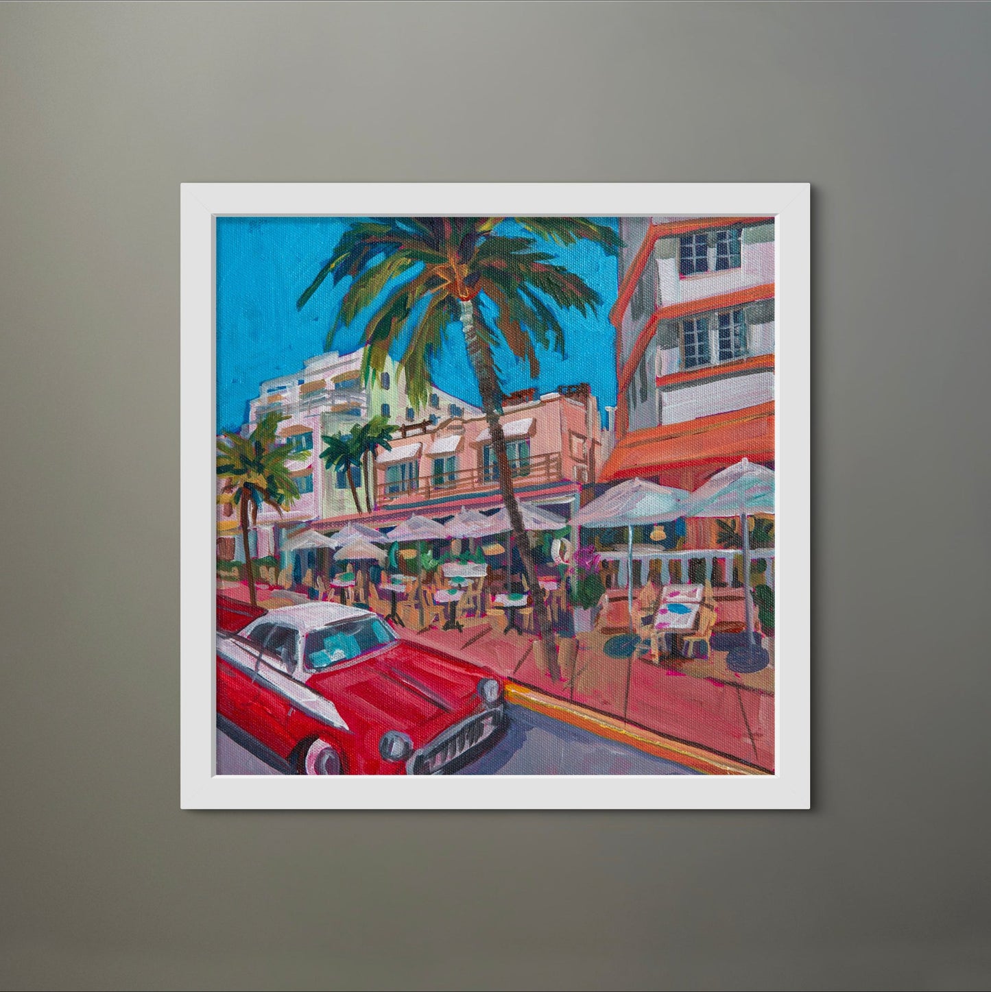 square painting of street scene in Miami, in white frame on grey wall. 