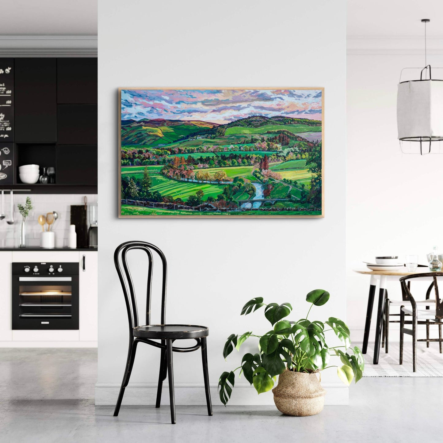 Contrast of a white kitchen dining area with black accents and a vibrant colorful painting with greens showing a landscape of rolling hills and fields of farmland 