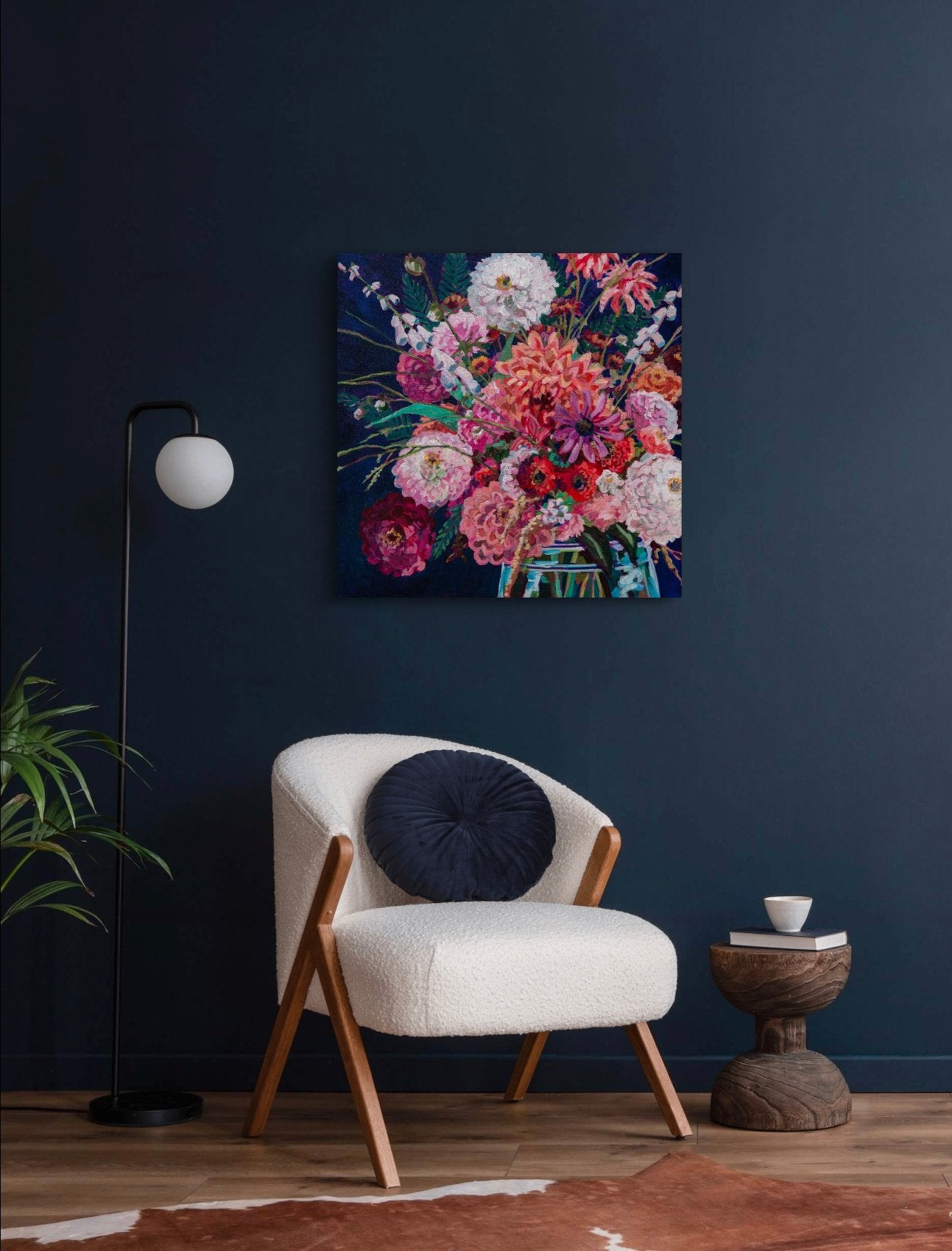 room with navy walls, modern cream chair, lamp and small table, with a vibrant square painting of bouquet of colorful flowers t