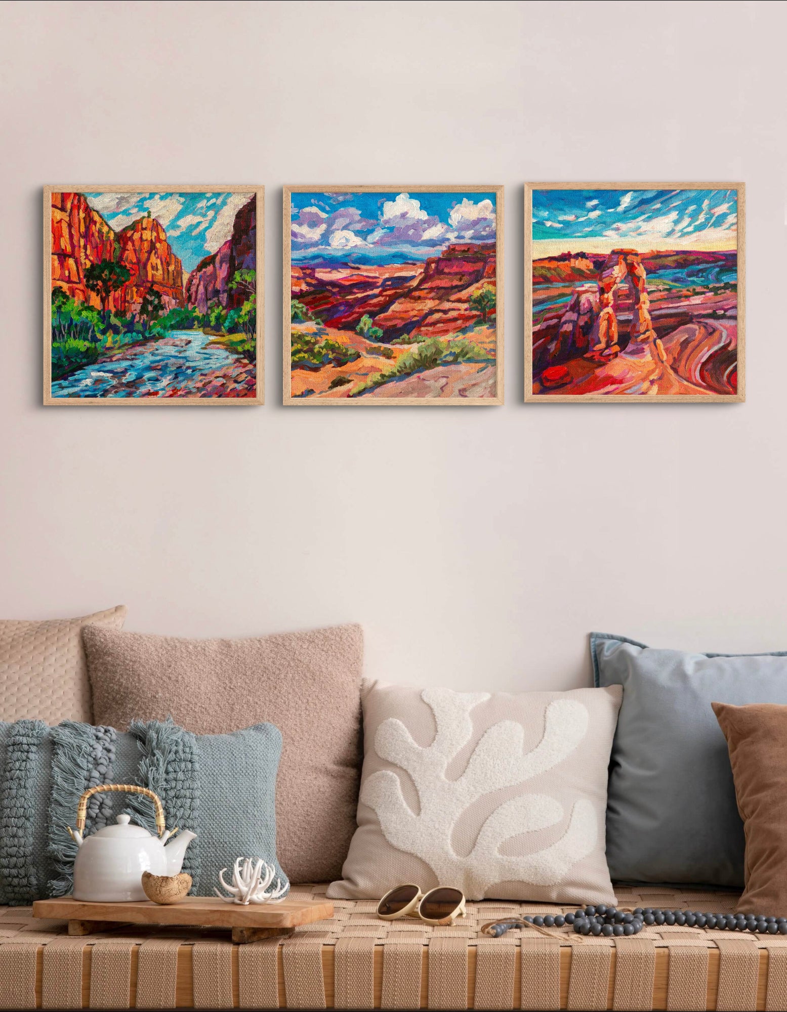 three southwest landscape paintings square of national parks, Zion, Canyonlands and Arches in front of bench with tan and blue pillows and decor