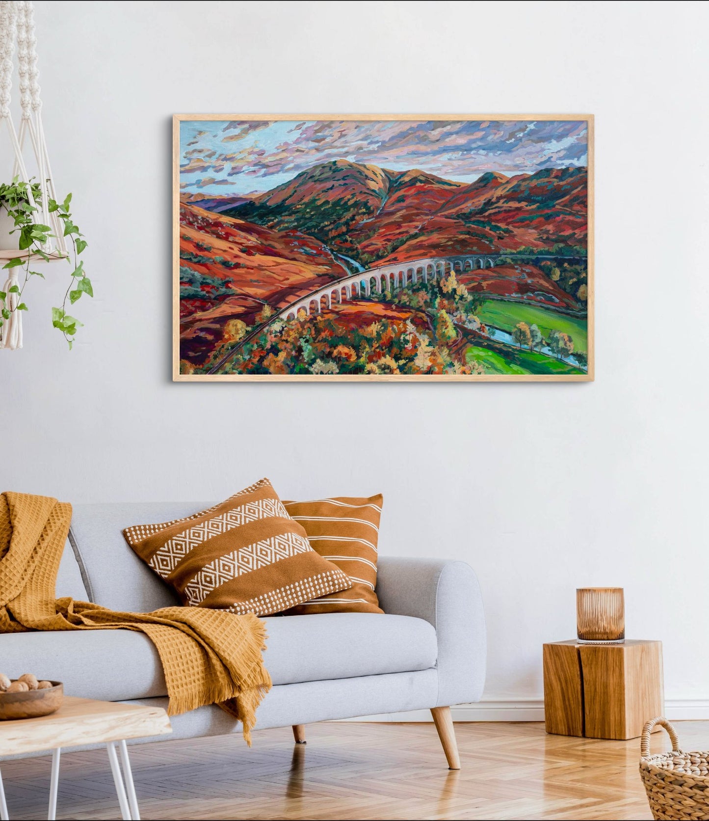 Bright room with white couch and accessories in rust wood and mustard colors, painting on wall is the statement focal point, large-scale impressionist landscape of mountains with a railway dissecting the scene.