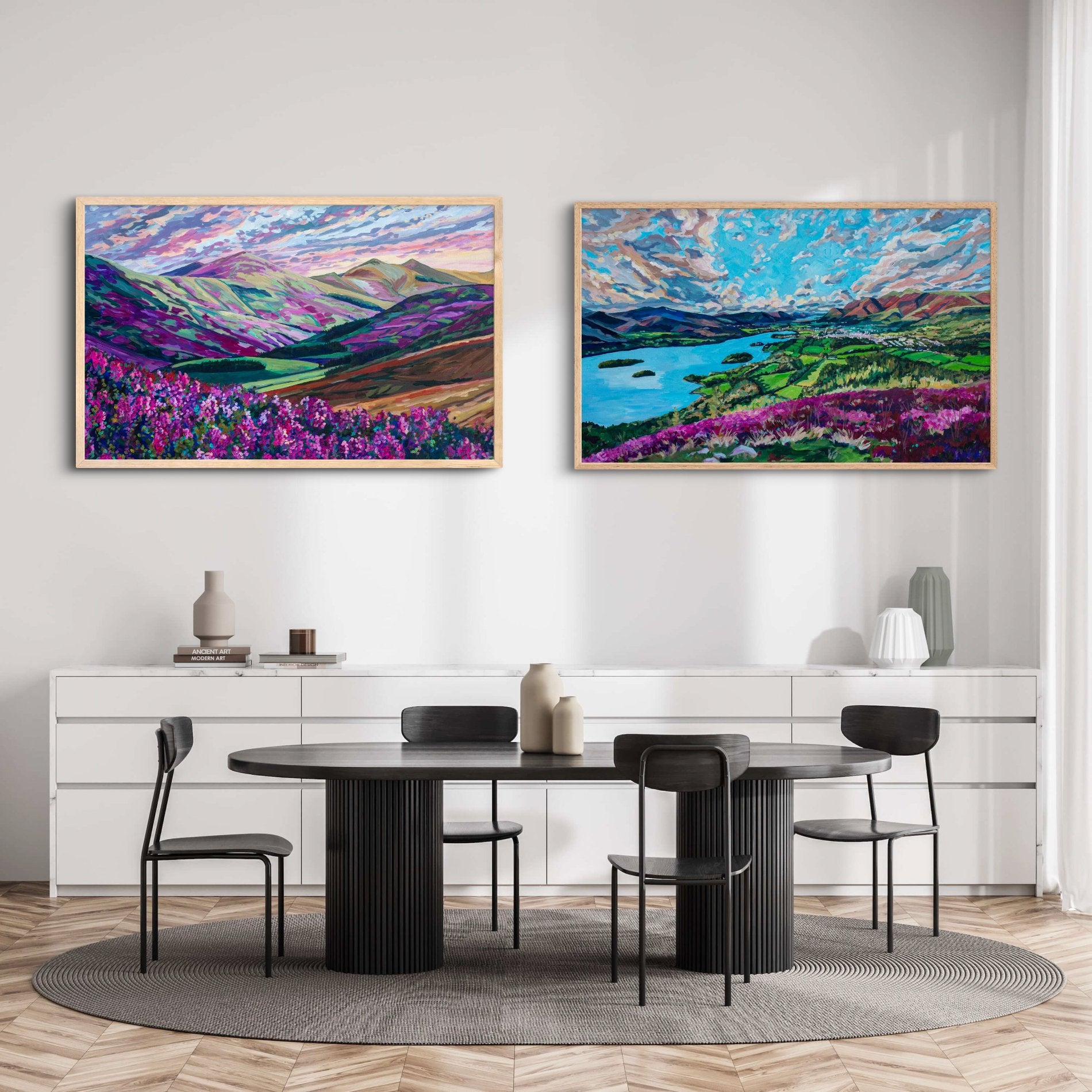 Two large landscape paintings of vibrant landscapes in the United Kingdom on a wall of neutral dining room with white shelves, vases and a modern dark brown/black dining table with chairs.