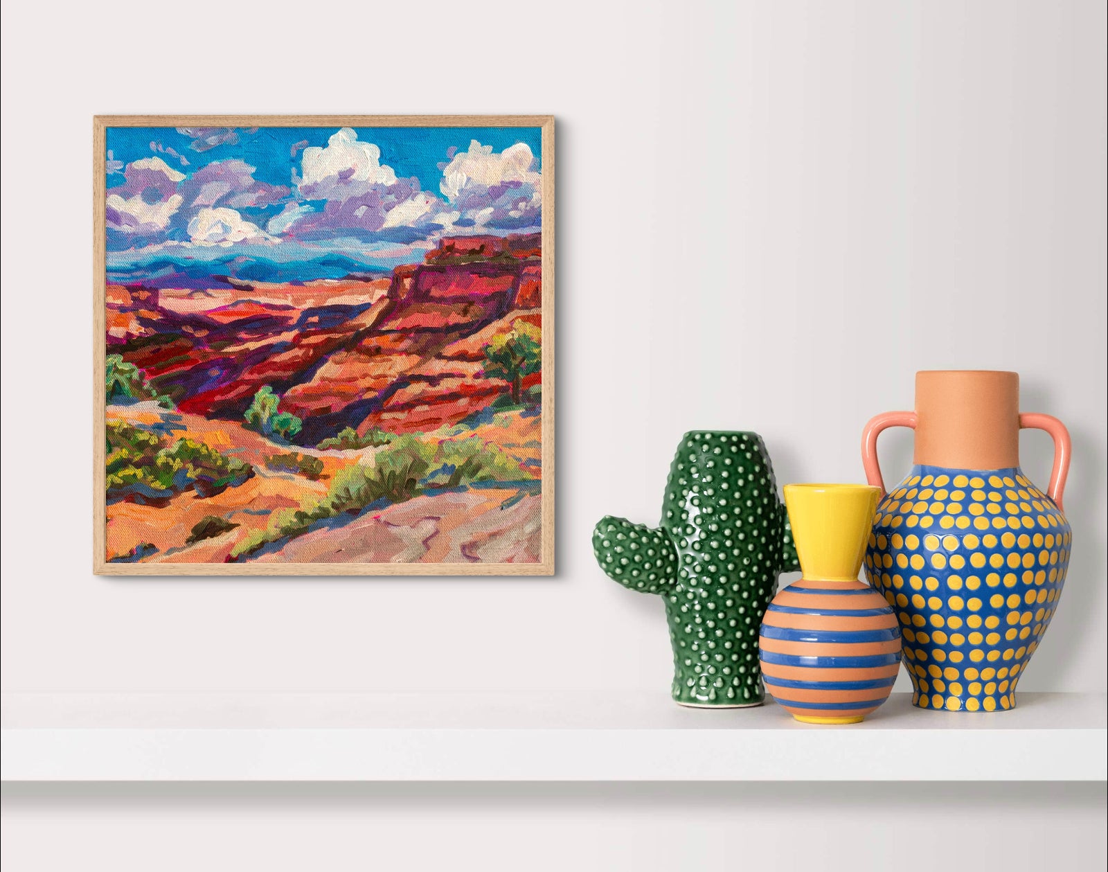 Modern landscape painting of Canyonlands national park in moab Utah above shelf with colorful pottery.