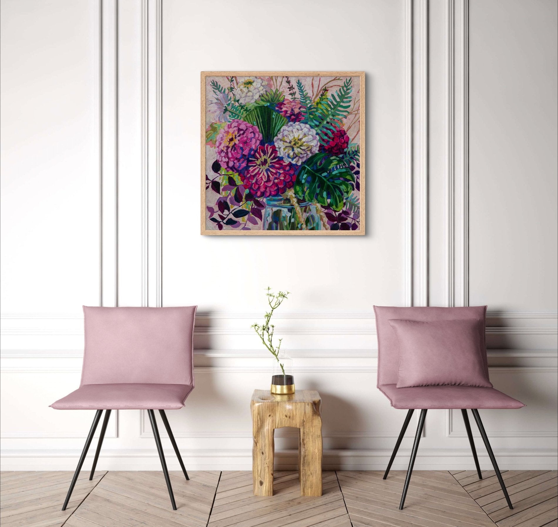 White room with traditional molding on walls and bright floral still life painting in modern impressionist style on wall above two modern pink chairs and small wood table.