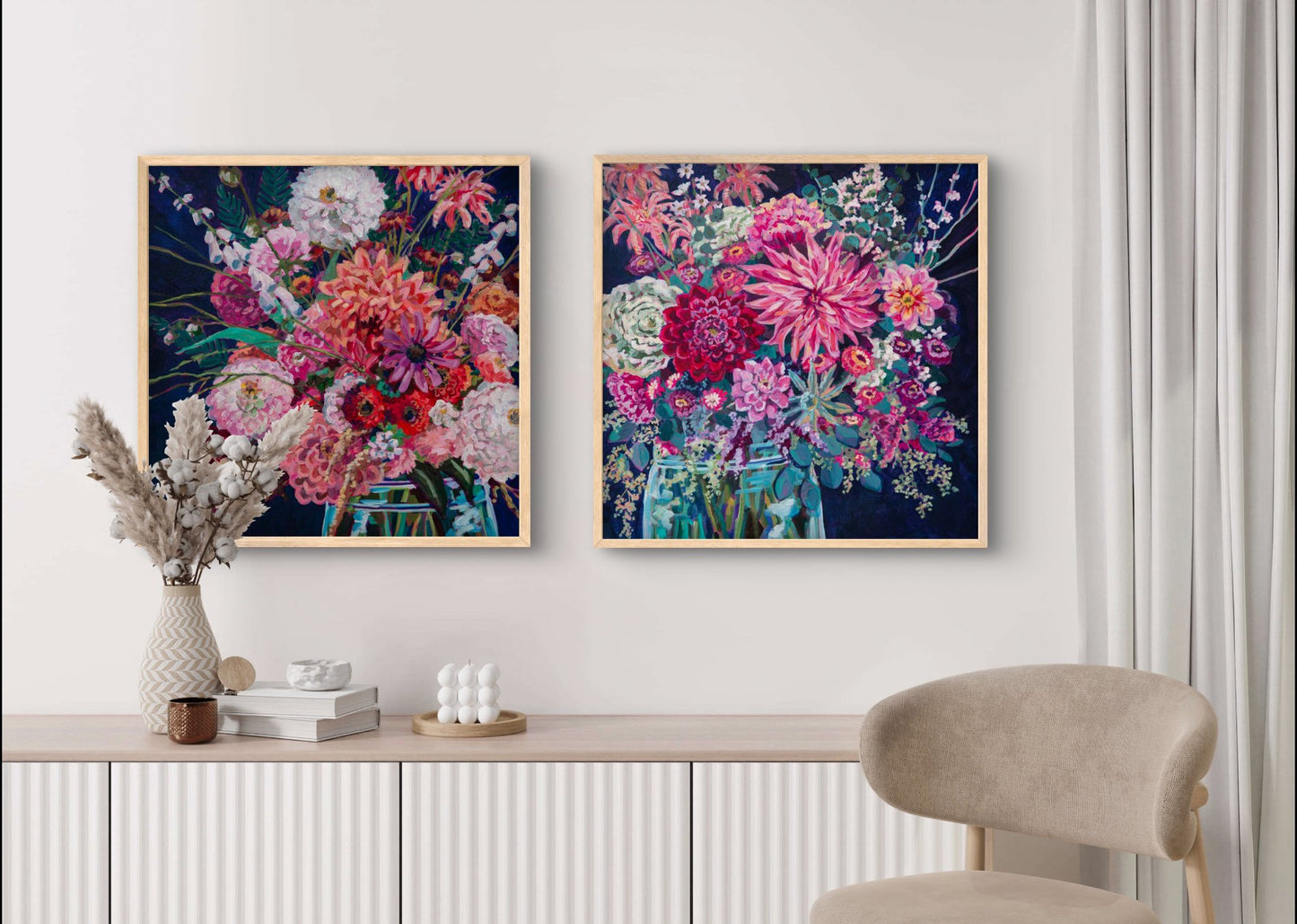 Two floral still life square modern paintings with rich warm colors contrasted with a dramatic navy background on wall of neutral room with tan chair and wall shelf.