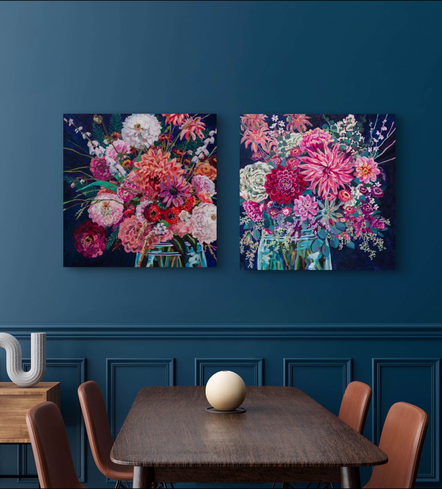 Two large square paintings of colorful floral arrangements in glass vases done in a modern expressive style in modern dining room with navy walls and molding.