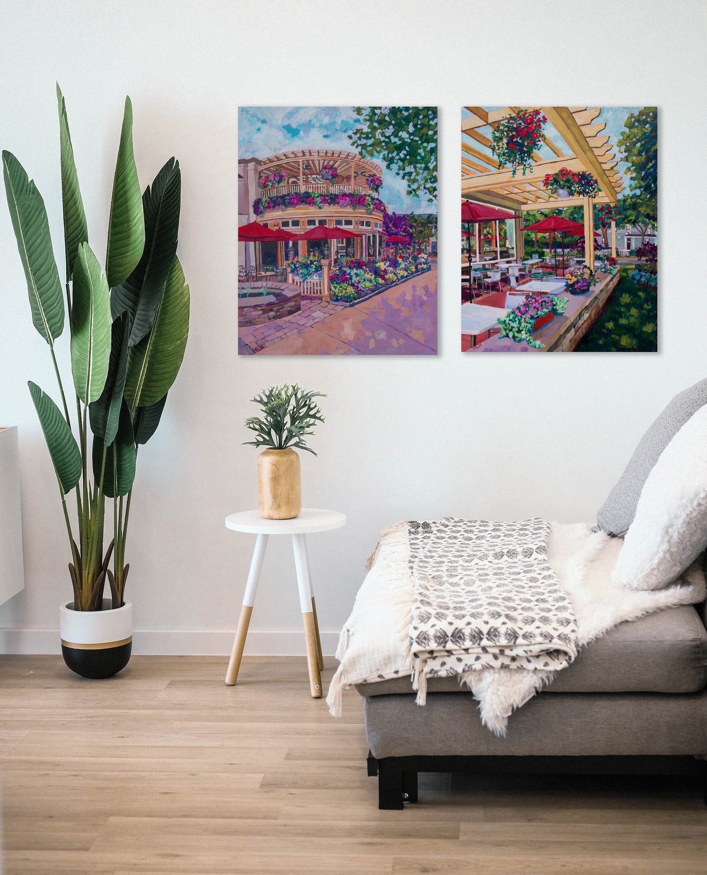 Two large original paintings of cafes from Niagara on the the Lake Canada in a living room setting with plants