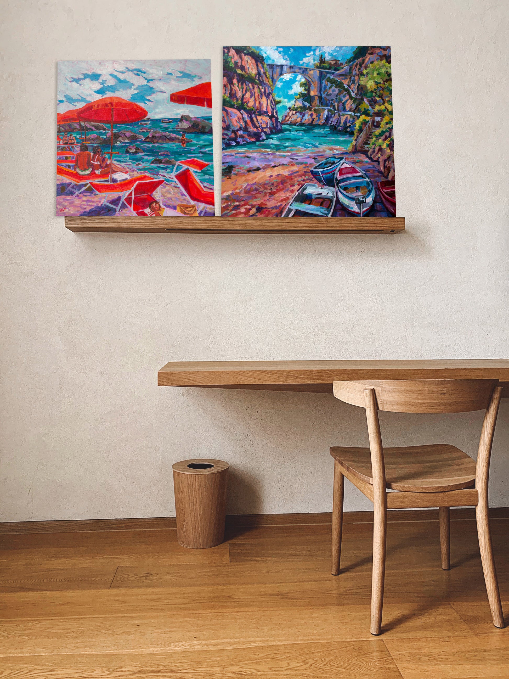 two paintings of the amalfi coast on shelf with desk