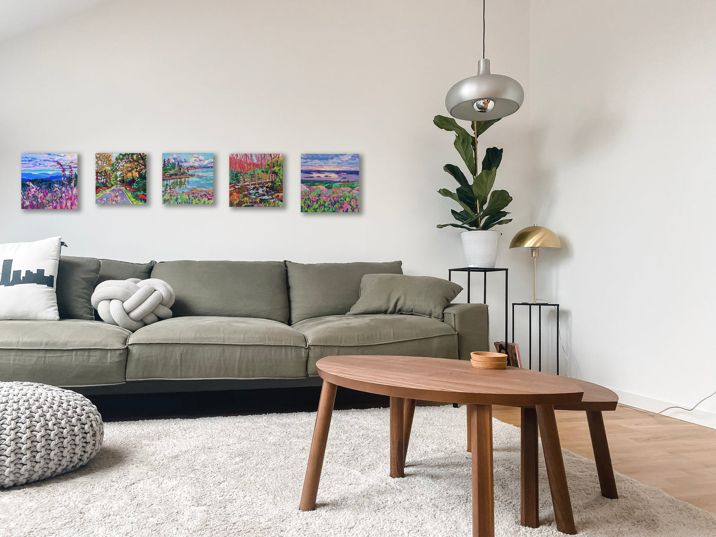 5 different small paintings on wall of living room behind a couch with table