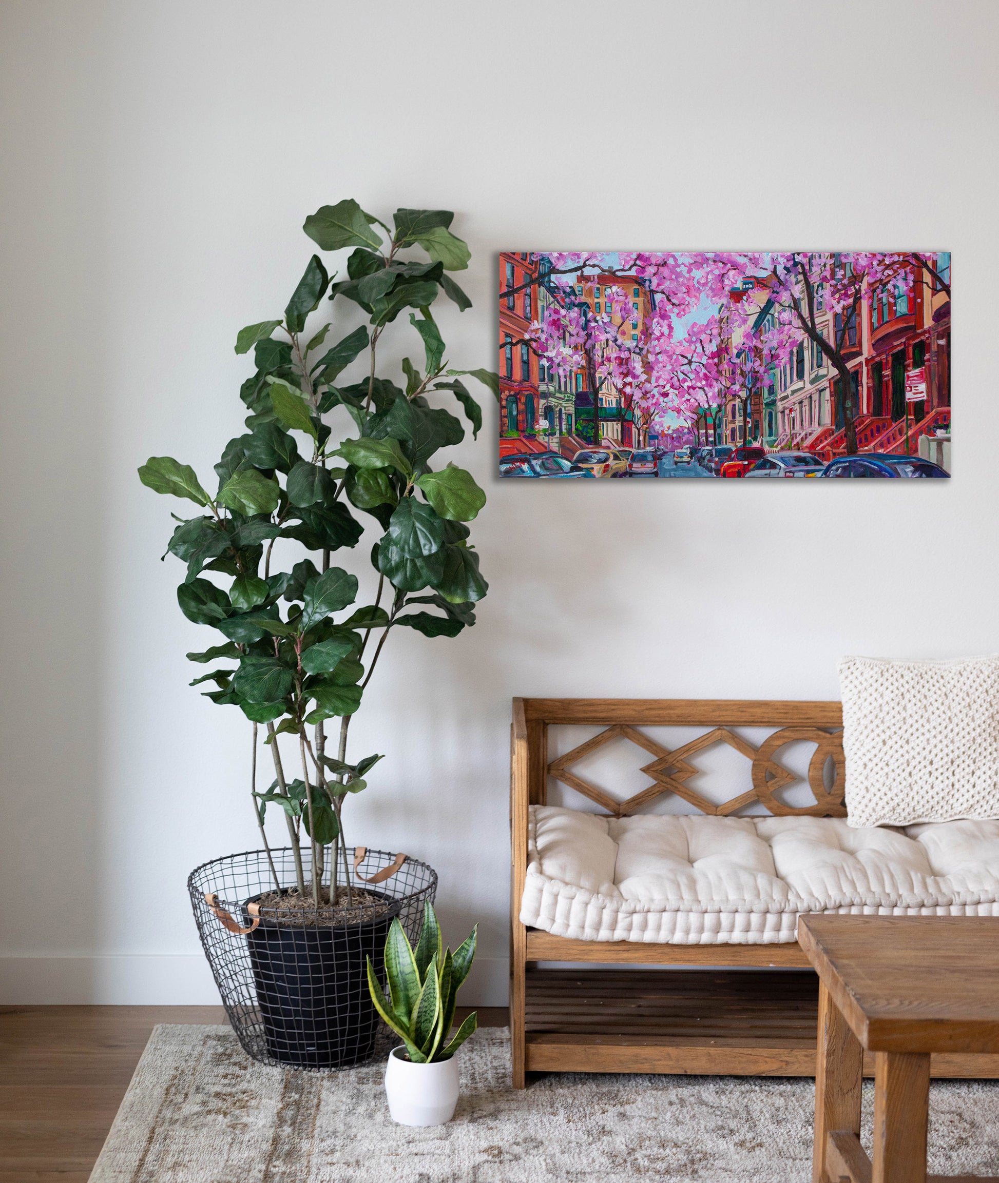 Painting hanging on wall with bench and tree: Vibrant street scene painting of NYC in spring with cherry blossoms in bloom and brownstone buildings.